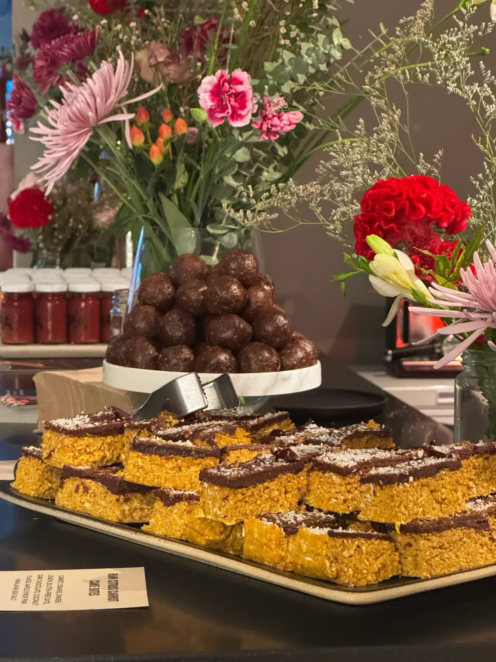Energy balls on a cake stand above a tray of chocolate-topped bars at an Aura event