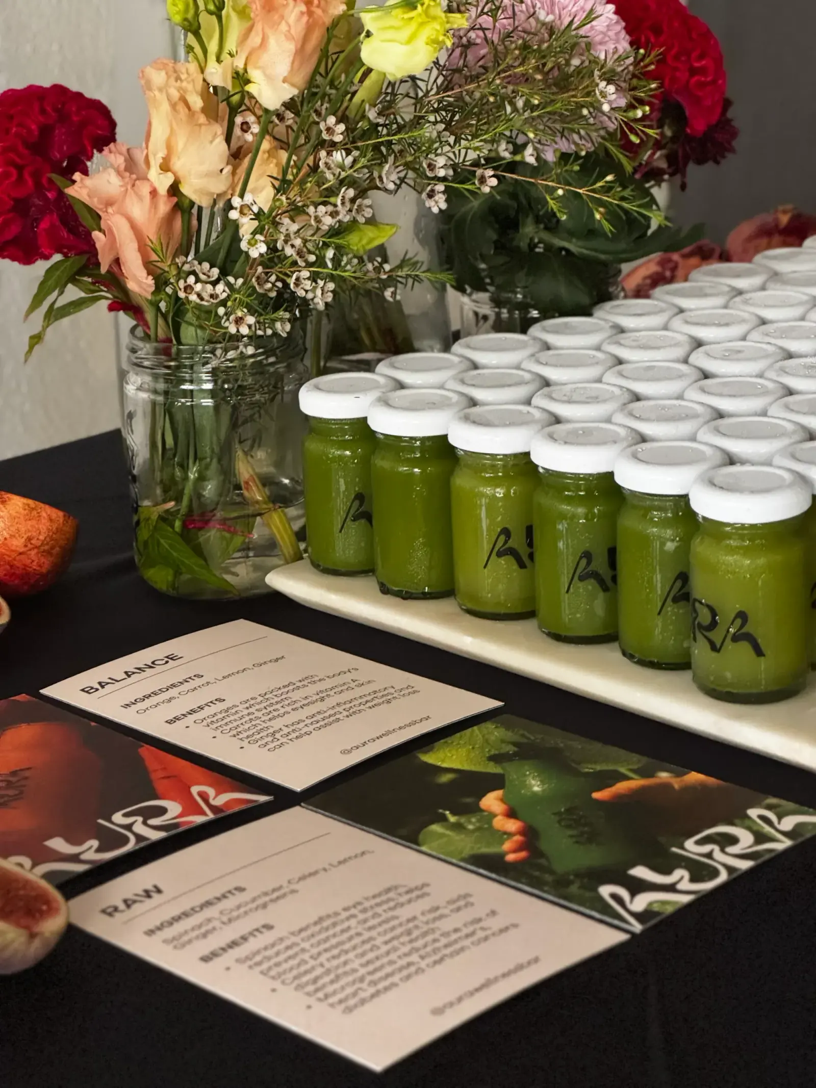 Green cold-pressed juice in small glass bottles beside RAW and BALANCE ingredient cards