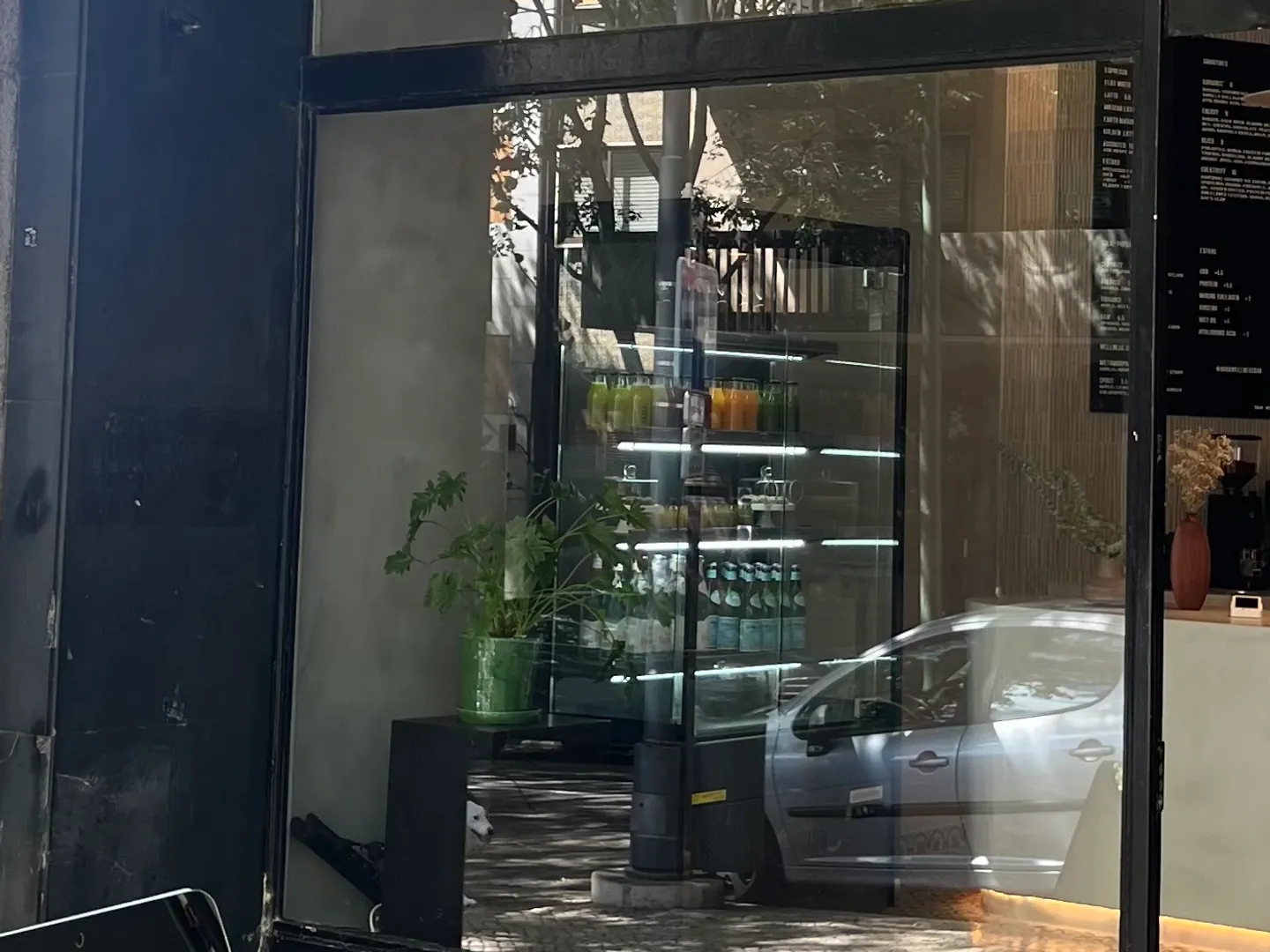 Aura Wellness Bar's shopfront on R. Domingos Sequeira in Campo de Ourique, with the juice fridge and the menu board seen through the window