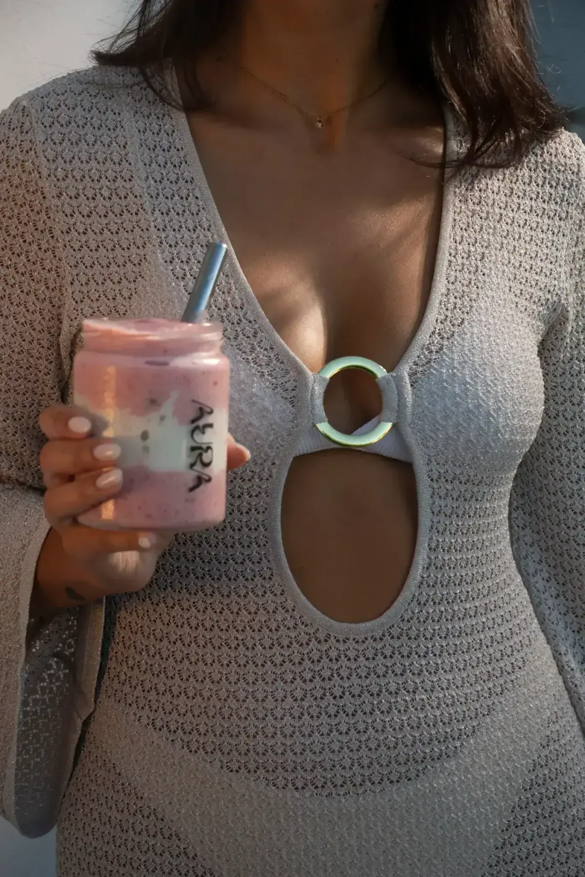 Pessoa a segurar um smoothie rosa da Aura num frasco de vidro com palhinha de metal